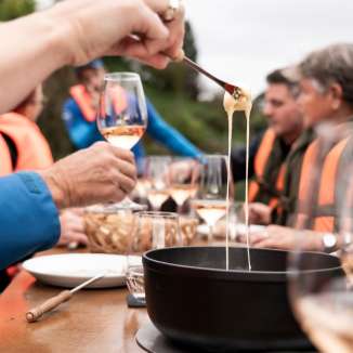 Gäste geniessen gemeinsam Käsefondue und Wein bei einer Flussfahrt auf der Aare.