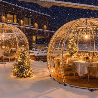 Beleuchtete Fondue-Iglus der Schifflaende in verschneiter Winterlandschaft mit festlich gedeckten Tischen.