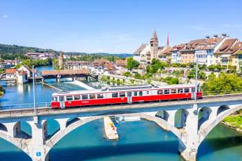 Rot-weisser Zug auf der Eisenbahnbruecke ueber die Reuss vor der historischen Altstadt von Bremgarten.