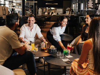 Zwei Männer und zwei Frauen sitzen in einer gemütlichen Runde am Loungetisch zum Aperitivo im Restaurant TYDE in der Therme Fortyseven in Baden