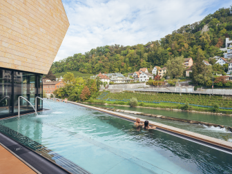 Ein Pärchen unterhält sich gemütlich am Beckenrand im Aussenbecken in der Therme FORTYSEVEN in Baden und geniesst dabei die Aussicht auf die Limmat.