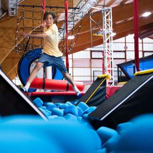 Jugendlicher springt in der Jump Factory Wohlen über einen Hindernisparcours mit Schaumstoffbecken, Rampen und Kletterelementen.