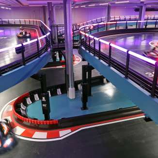 Mehrere E-Go-Karts fahren auf einer beleuchteten Indoor-Rennstrecke mit Kurven und mehreren Ebenen im Cinema 8 in Schöftland