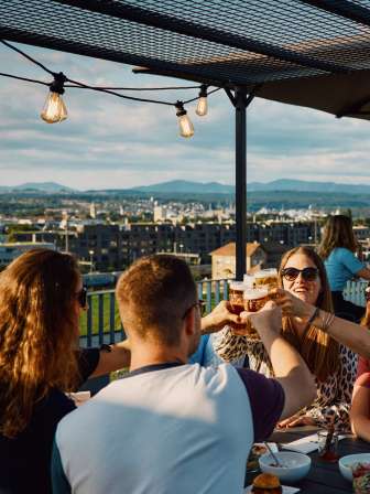 Eine Gruppe von vier Personen stösst auf der Dachterrasse des Feldschösschens mit einem Glas Bier an.