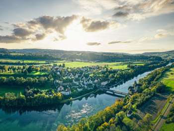 stimmungsvolle luftaufnahme von kaiserstuhl im aargau mit blick auf die altstadt, die bruecke ueber den rhein und die weiten felder in warmem abendlicht.