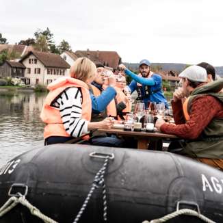 Gruppe geniesst gemeinsam Fondue und Wein auf einem Boot auf der Aare im Aargau.