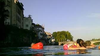 Personen schwimmen an der Altstadt von Rheinfelden vorbei.