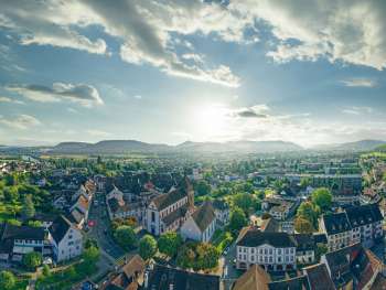 grossartige luftaufnahme von bad zurzach im aargau mit blick ueber die altstadt, kirche, wohnhaeuser und die weite landschaft unter einem hellen himmel.