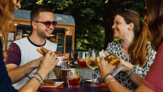 Vier Personen sitzen an einem kleinen Tisch bei einer Buvette und essen etwas.