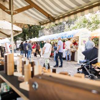 besucher auf einem genussmarkt mit verschiedenen marktstaenden und regionalen angeboten.