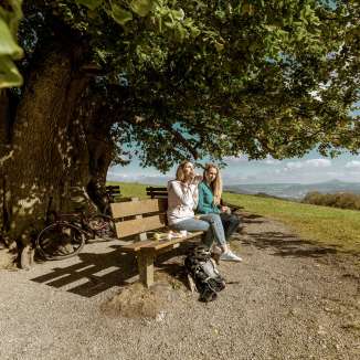 Zwei Frauen machen eine Picknickpause bei der Linner Linde und geniessen regionale Köstlichkeiten