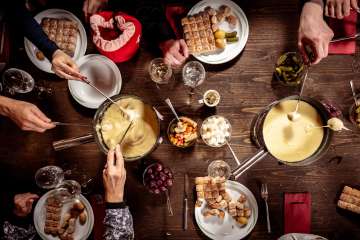 Mehrere Personen geniessen gemeinsam Käsefondue mit Brot und Beilagen an einem gedeckten Holztisch im Tägi Wettingen