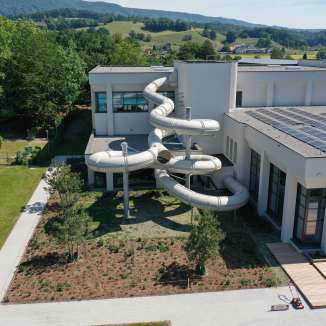 Aussenansicht des Taegi Wettingen mit grosser, geschwungener Wasserrutschbahn und Solaranlage auf dem Dach.