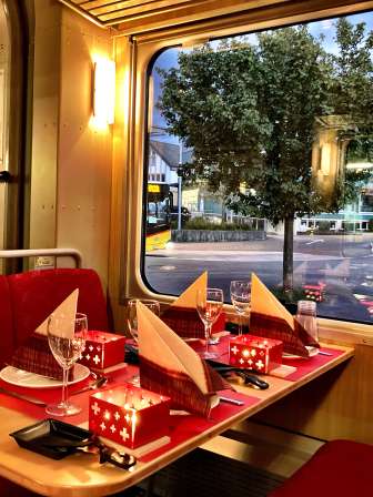 Zwei Personen geniessen gemeinsam ein Kaesefondue waehrend einer abendlichen Fahrt im Zug.