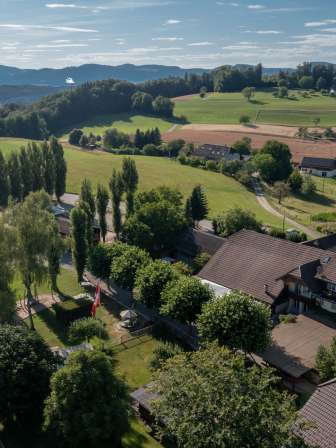 luftaufnahme des ruetihofs in graenichen mit hofanlage, umgeben von gruenen wiesen, baeumen und der huelligen landschaft des aargaus.