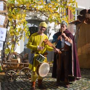Altstadt Bremgarten mit zwei Personen, die mittelalterliche Kleidung tragen und verschiedene Instrumente spielen.