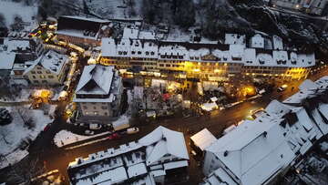 Luftaufnahme von Aarburg bei Dämmerung mit verschneiten Dächern, beleuchteten Marktständen und zahlreichen Besuchern am Anlass «Aarburg leuchtet».