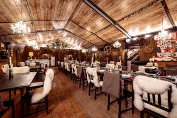 White Saloon im Tägi Wettingen mit gedeckten Holztischen, Fellauflagen und warmen Kronleuchtern.